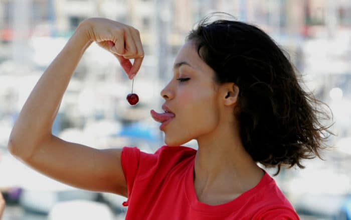 photo of Rosario Dawson sticking her tongue out at a cherry and wearing a red shirt