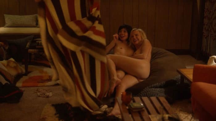 Kate Micucci sitting on a couch with woman completely nude