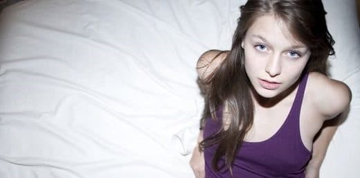 Melissa Benoist sitting on bed in a purple dress