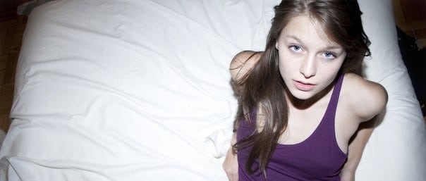 Melissa Benoist sitting on bed in a purple dress