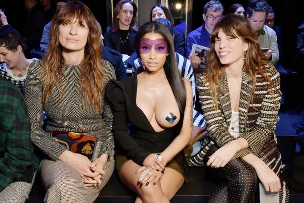 Nicki Minaj sitting down in black dress that exposes her boob during fashion week