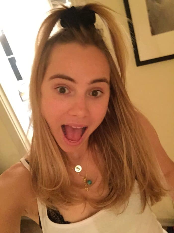 Suki Waterhouse taking a selfie with mouth open and hair in a top knot