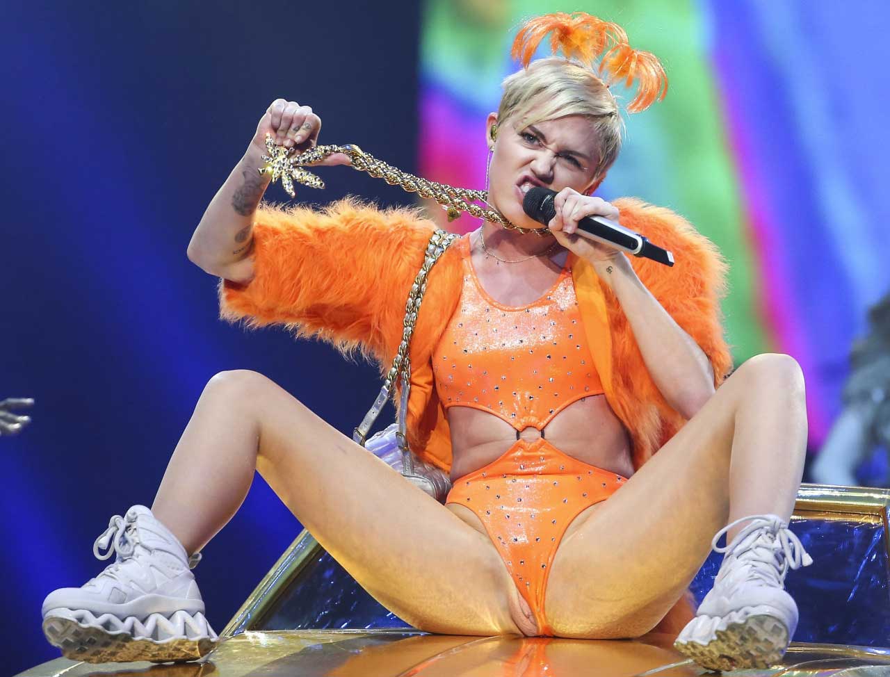 Miley Cyrus on stage wearing an orange body suite legs spread