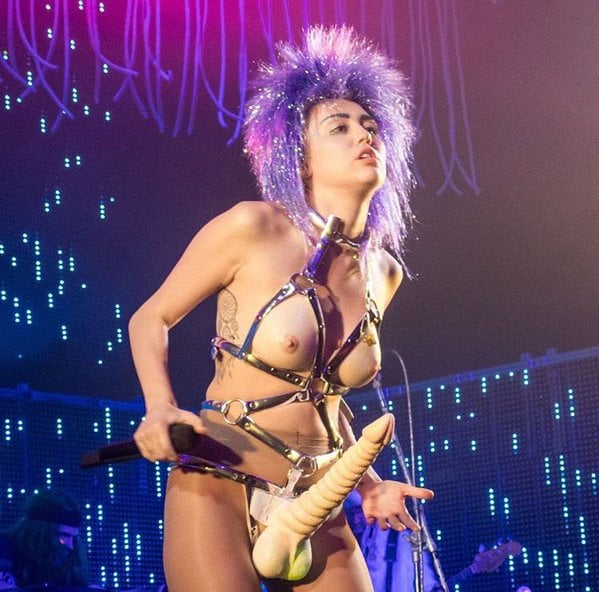 Miley Cyrus wearing a purple wig and strap on penis on stage