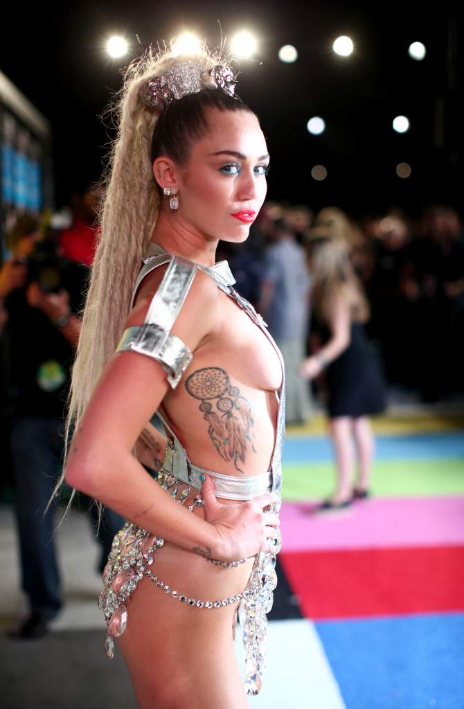 Miley Cyrus wearing a silver outfit side boob exposed