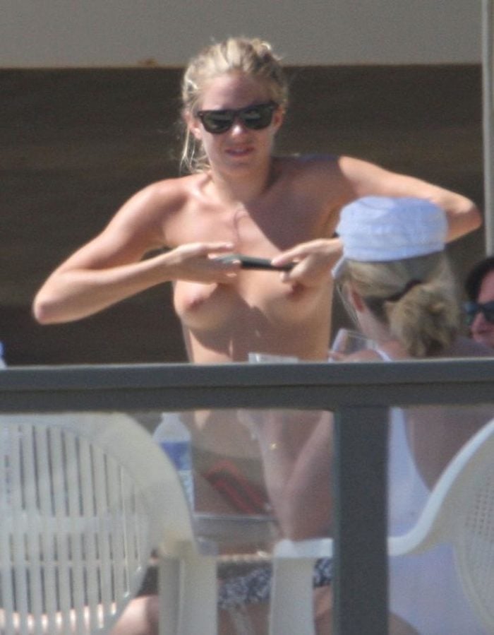 Sienna Miller pulling down her shirt on a balcony showing her nipples