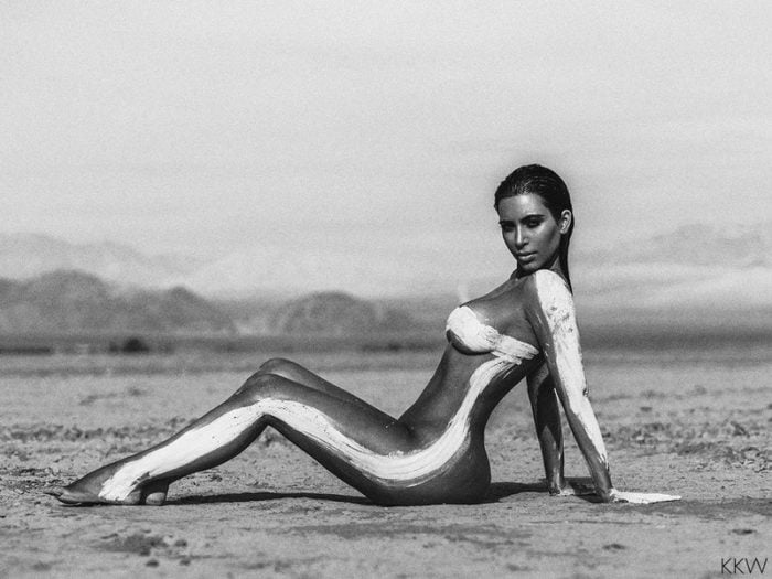 Kim Kardashian with ass sitting down in the desert and a white stripe on her body