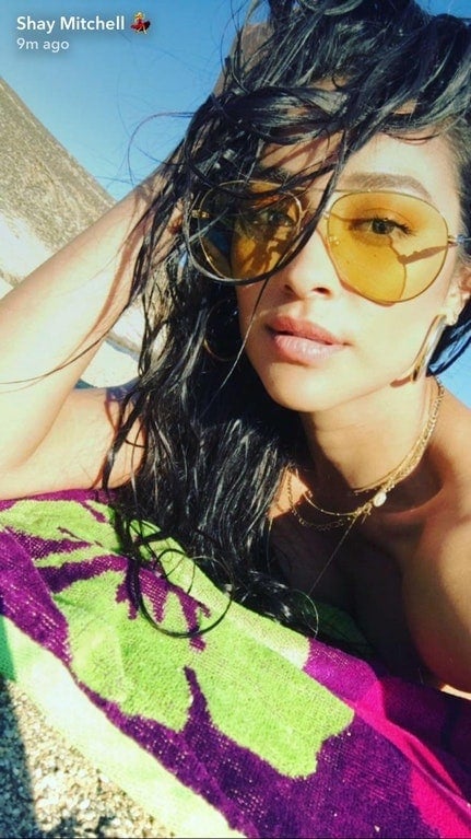 Shay Mitchell wearing yellow sunglasses and laying on a beach towel snapchat